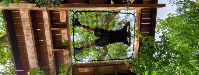 Un homme qui se repose dans un filet intégré dans une terrasse suspendue dans les arbres.
