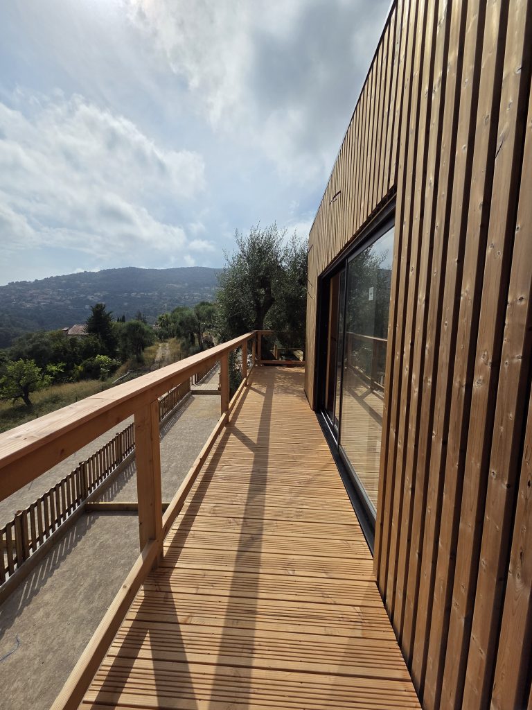 Terrasse en bois longeant la baie vitrée du cabanon, vue sur les collines
