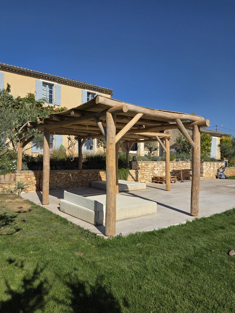 Pergola en rondins d’acacia entre pelouse et terrasse dallée